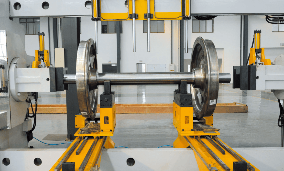 A railway wheel and axle set mounted on a yellow workshop machine